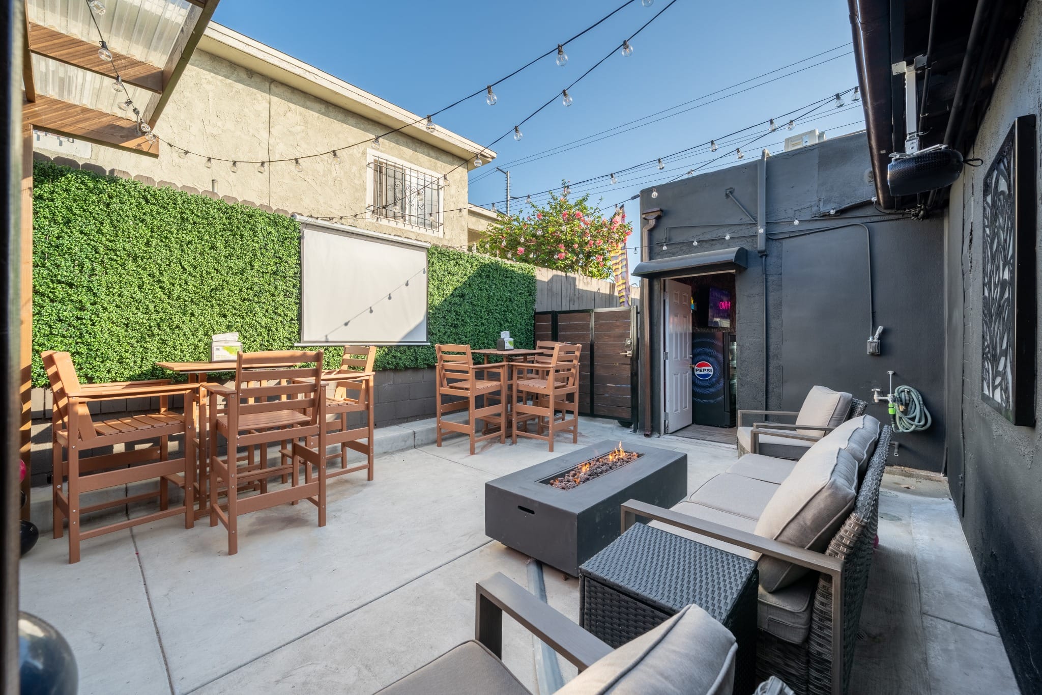 Covered patio with string lights, wooden tables, and lounge seating